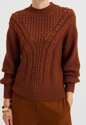 Brun strikket sweater med høj hals, der har kabelstrik mønstre og hulmønstret detaljer. Ribbet manchetter og kant, tekstureret stoffinish.