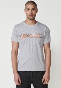 Gray cotton T-shirt featuring "KOBUSHBRAND" logo in black and orange print. Short sleeves and crew neck with a casual fit.