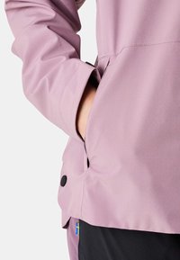Lahka vijolična vodoodporna jakna z zadrgo na žepu in črnimi gumbi na manšetah. Gladek teksturiran material in sproščen kroj.