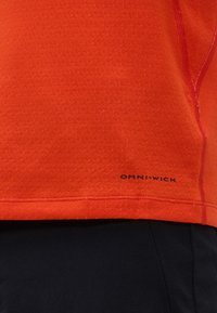 Κοντινό πλάνο κόκκινου υφάσματος με υφή και το κείμενο "OMNI-WICK" κοντά στο τελείωμα, πάνω από μαύρο ύφασμα ένδυσης.