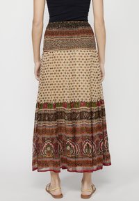 Maxi skirt in beige and red with floral and geometric prints. Features a smocked waistband and layered hem. Lightweight, flowy fabric.