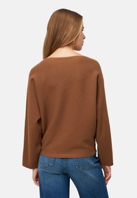 Pull marron côtelé avec un large col et des manches longues, assorti à un jean en denim bleu, vu de dos.