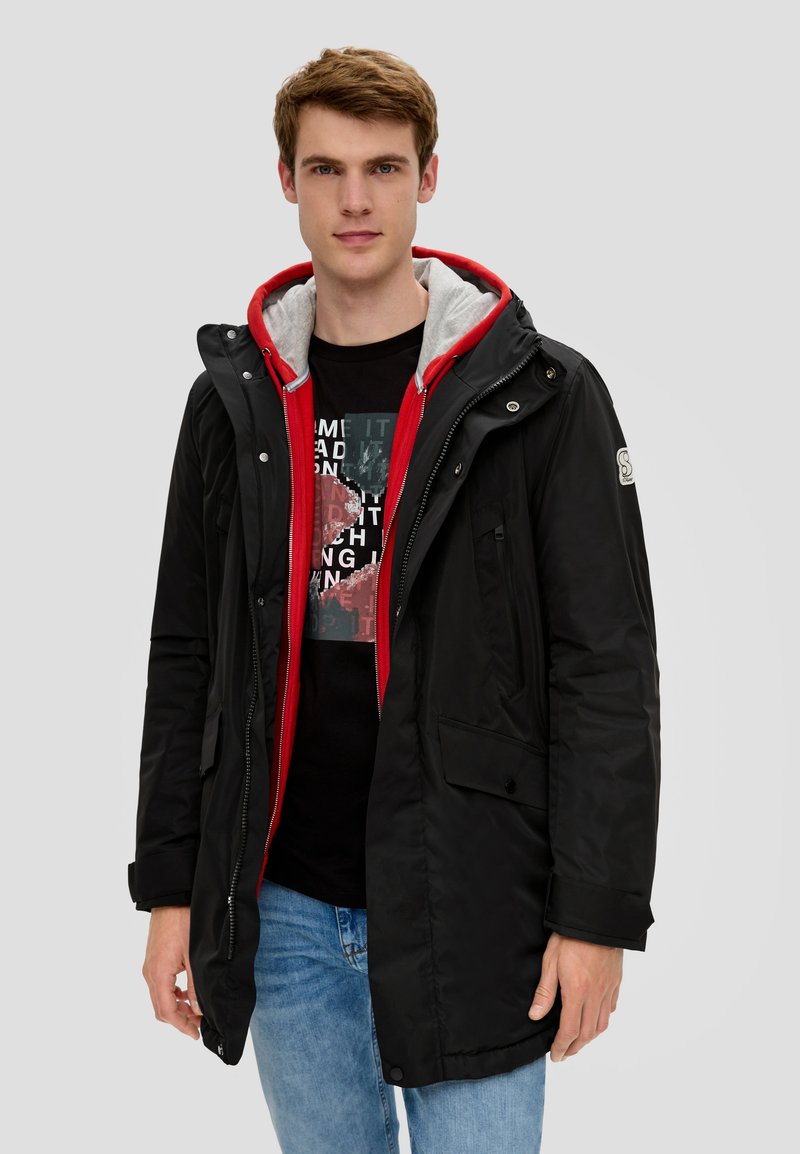 Schwarze, kapuzenjacke mit wasserabweisendem Außenmaterial, rotem und grauem Innenfutter, knöpfen für die Taschen und einem Reißverschluss vorne.