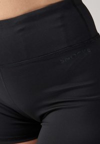 Shorts neri a vita alta con una superficie liscia. Presentano un sottile logo del brand impresso sulla vita e cuciture piatte per il massimo comfort.