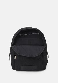 Czarna pikowana plecak z zamkiem błyskawicznym w głównym komorze i przedniej kieszeni. Wnętrze ma tkaninową wiadomość i płaską kieszeń. Miękka tekstura.