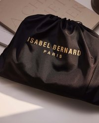 Black satin drawstring pouch featuring gold embossed text "ISABEL BERNARD PARIS." Smooth texture with a gathered opening, minimalistic design.