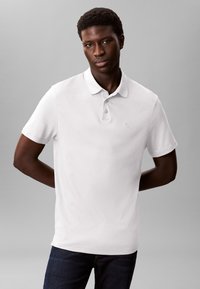 White polo shirt made of cotton, featuring a classic collar and three buttons, paired with dark blue denim jeans.