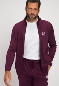 Chaqueta atlética burdeos con cremallera, detalles en blanco y logo en el pecho; combinada con pantalones a juego. Tejido lisos y elástico; ajuste casual.