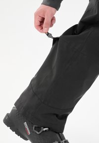 Svarta vattentäta byxor i hållbart material, med justerbar elastisk snodd och sömlös design, tillsammans med svarta utomhusskor.