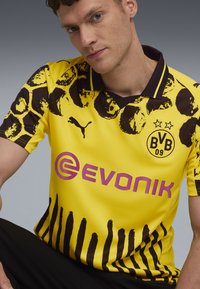 Tricou de fotbal galben cu imprimeu de leopard negru și detalii în dungi. Prezintă logo-ul Puma, emblema Borussia Dortmund și logo-ul sponsorului Evonik.