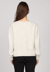 Pull léger gris clair avec un col rond, des manches longues et des bords côtes. Le tissu semble doux et confortable avec une finition texturée.