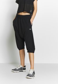 Schwarze, cropped Sweatpants mit elastischem Bund und Seitentaschen, verfügen über eng anliegende Bündchen. Kombiniert mit schwarz-weißen Sportschuhen.