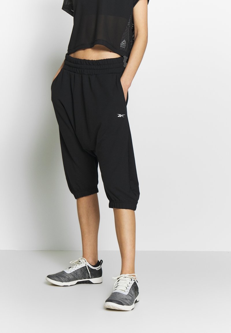 Schwarze, cropped Sweatpants mit elastischem Bund und Seitentaschen, verfügen über eng anliegende Bündchen. Kombiniert mit schwarz-weißen Sportschuhen.