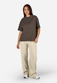 Brązowy oversize'owy t-shirt z krótkimi rękawami, w połączeniu z jasnobeżowymi, fakturowanymi spodniami o szerokich nogawkach i białymi butami sportowymi.