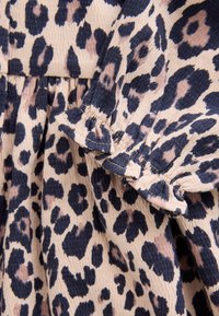 Leopardenmusterstoff in Beige- und Marineblau-Tönen. Die strukturierte Oberfläche zeichnet sich durch Rüschenärmel und geraffte Details aus.