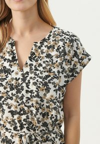 Robe à motif floral avec décolleté en V, manches courtes et poche. Les couleurs incluent crème, noir et moutarde avec un tissu texturé.