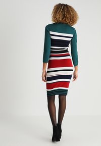 Stickad klänning med tealfärgade ärmar, med horisontella ränder i röd, vit, marinblå och grön. Tätt sittande silhuett, knälång design.