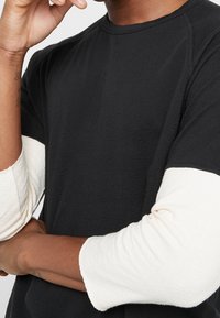 Schwarzes kurzärmliges T-Shirt mit strukturiertem Finish und kontrastierenden cremefarbenen langen Ärmeln. Reguläre Passform mit rundem Halsausschnitt.