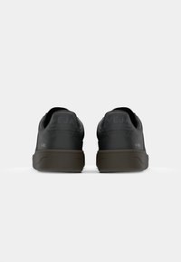 Sorte lær sneakers med mørkebrune gummisåler, hælflapper og præget branding. Rund tå og minimalistisk design.