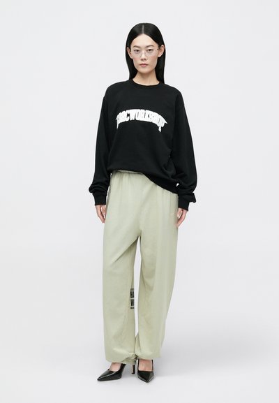 Melnas pārsteidzoši lielas kapuces krekls ar baltu tekstu, gaiši zaļa platās bikses un smailas melnas kurpes. Skatu punkta, stūra brillēm pabeidz izskatu.