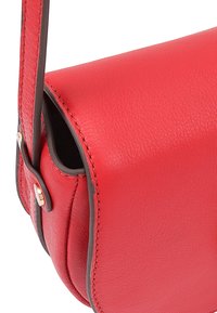 Rode leren crossbody tas met een gladde textuur, voorzien van contrasterende donkere accenten en goudkleurige hardware. Ronde vorm en een veilige sluiting.