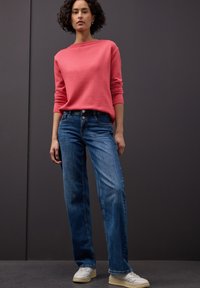 Pull en maille corail, jean bleu droit et baskets blanches. Design simple, texture douce et coupe décontractée mises en valeur sur un fond sombre.