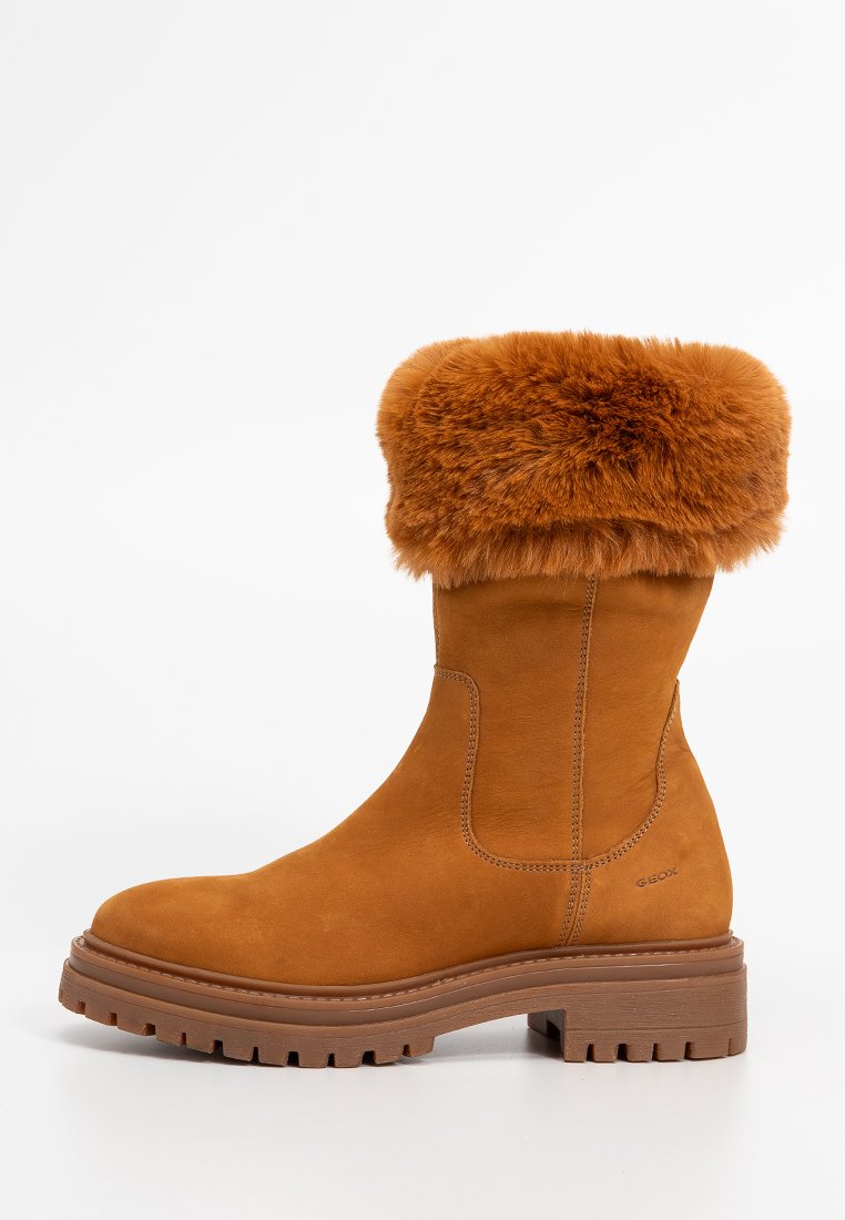 Botín tobillo de ante color marrón claro con un puño de piel de pelo marrón, suela de goma texturizada y paneles elásticos laterales para facilitar el uso. Logo de la marca en el lateral.