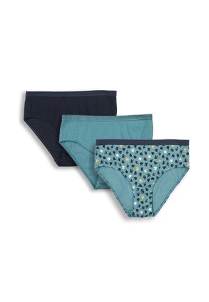 Junge Frau steht barfuß in einem passenden blauen gemusterten Bralette und hoch taillierten Unterwäsche vor einem schlichten hellen Hintergrund.