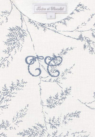 Tessuto bianco con delicati motivi a ramo botanico grigi, iniziali blu ricamate "T E" e un'etichetta "Tartine et Chocolat" con taglia T1.