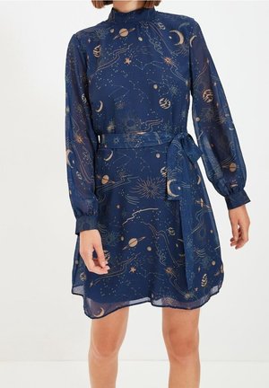 Navyblaudekleid mit langen Ärmeln, himmlischem Druck, hohem Kragen, Taillengürtel und leicht durchscheinendem Stoff an einer stehenden Person.