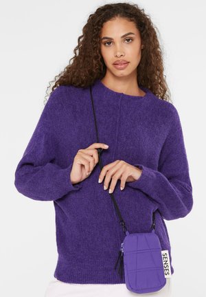 Lila gestrickter Pullover mit Rundhalsausschnitt. Verfügt über lange Ärmel und eine weiche Textur. Begleitet von einer kleinen lila Umhängetasche mit einem Anhänger.