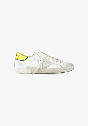 Sneaker bassa bianca con suola beige, lacci beige, punta in suede grigia e linguetta del tallone gialla neon con rifiniture e testo neri.