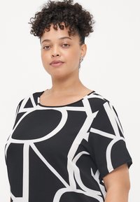 Black top featuring bold white geometric patterns, short sleeves, a round neckline, and a textured fabric.