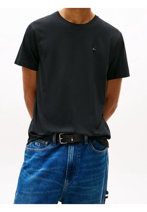 Camiseta de algodón negra con cuello redondo, mangas cortas y un pequeño logo en el pecho, combinada con pantalones de mezclilla azules y un cinturón negro.