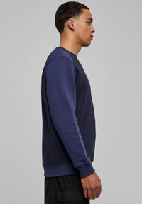 Tumesinist värvi dressipluus pikkade varrukatega, soonikkoes mansettide ja alläärega. Sile tekstuur, minimalistlik disain, näidates mudeli külgprofiili.