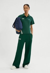 Zielona koszulka polo z krótkim rękawem, z kołnierzykiem; w komplecie z pasującymi zielonymi spodniami z białymi bocznymi paskami i naszywką z logo. Ciemnoniebieska torba.