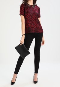 Kortærmet rød leopardprint bluse med en krave i sort lace, parret med sorte skinny jeans og en sort clutch, iført sorte hæle.