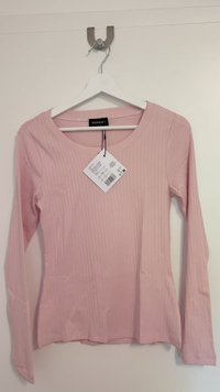 Blusa de manga longa rosa suave com textura canelada e decote arredondado. Pendura num cabide branco, com etiqueta anexada contendo informações de cuidados.