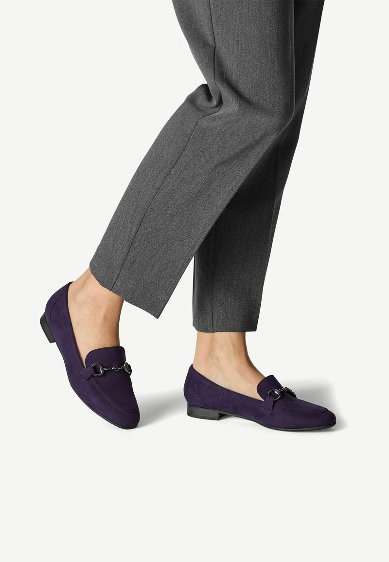 Loafers din suede violet cu vârf rectangular, dotati cu un accent decorativ dintr-un lanț metalic și un toc mic cu talpă înălțată, asortați cu pantaloni gri.