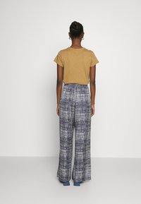 Geel shirt met korte mouwen gecombineerd met hooggetailleerde, wijde broek met een blauw-wit ruitpatroon.