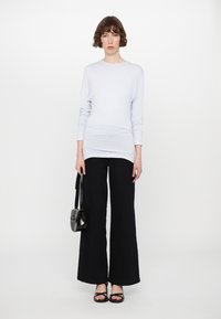 Maglietta azzurra chiara a maniche lunghe abbinata a pantaloni ampi neri a vita alta. La modella tiene una piccola borsa nera e indossa sandali neri.