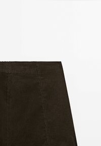Tissu en velours côtelé marron foncé avec côtes verticales et coutures distinctes sur une partie de vêtement.