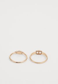 Deux anneaux en ton or, l'un avec un bandeau lisse et un design fantaisiste, l'autre présentant une forme ovale avec de petites pierres d'accent tout autour.