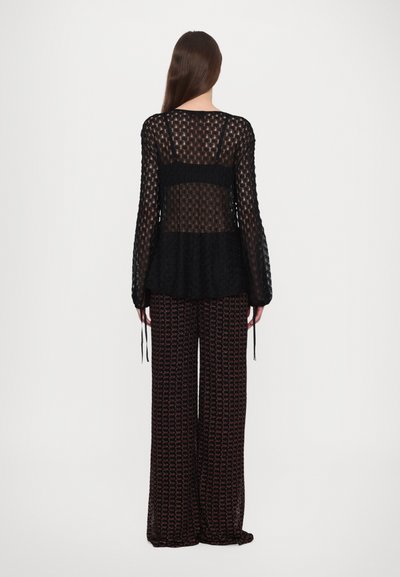 Top nero trasparente a maniche lunghe con un motivo a pois testurizzato, abbinato a pantaloni a gamba larga con un design geometrico rosa.