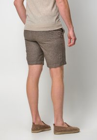 Brown linen shorts with turn-up hems, side pockets, and a textured finish, paired with brown slip-on shoes.