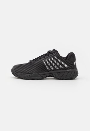 Zapatilla deportiva negra con un upper texturizado, que presenta acentos de franjas blancas, una suela acolchada y un diseño de punta redondeada.