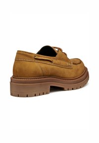 Mocasín de ante marrón con suela gruesa tipo lug, costura en la puntera y detalle de cordón de cuero alrededor del talón, en ángulo para mostrar el lado exterior y la suela.