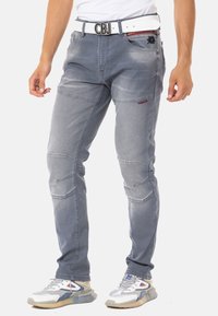 Graue Stretchjeans mit strukturierter Oberfläche, die über auffällige Nahtdetails und einen kontrastierenden weißen Gürtel mit Schnallenverschluss verfügen.