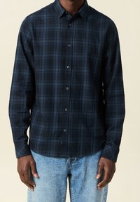 Marinblå rutig skjorta med krage som kan knäppas, långa ärmar och en mjuk tygstruktur, med mörkblå och ljusblå rutor.