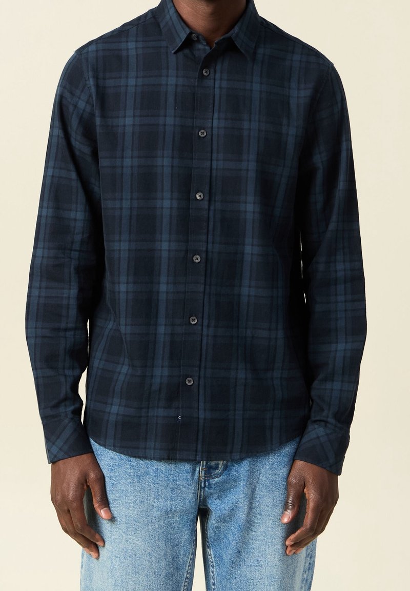 Marinblå rutig skjorta med krage som kan knäppas, långa ärmar och en mjuk tygstruktur, med mörkblå och ljusblå rutor.